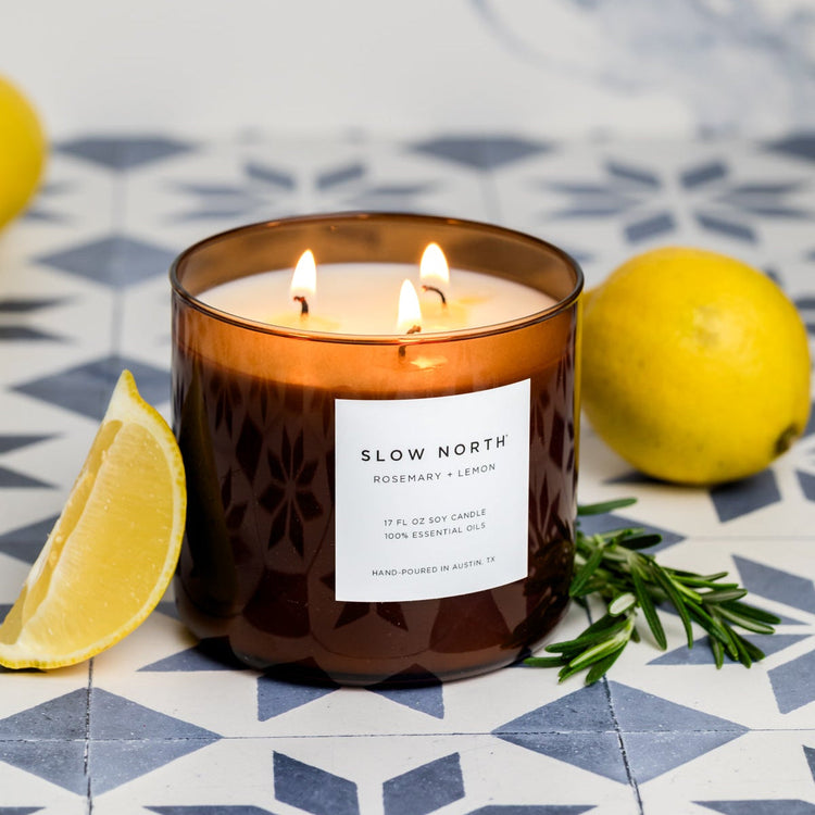 Rosemary and Lemon three-wick candle lit in an amber glass jar